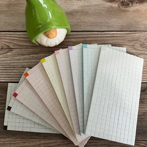 May include: A set of ten white ceramic tiles with a grid pattern. The tiles are arranged in a fan shape and have a variety of colored borders, including red, orange, yellow, light green, pink, purple, blue, and light blue.