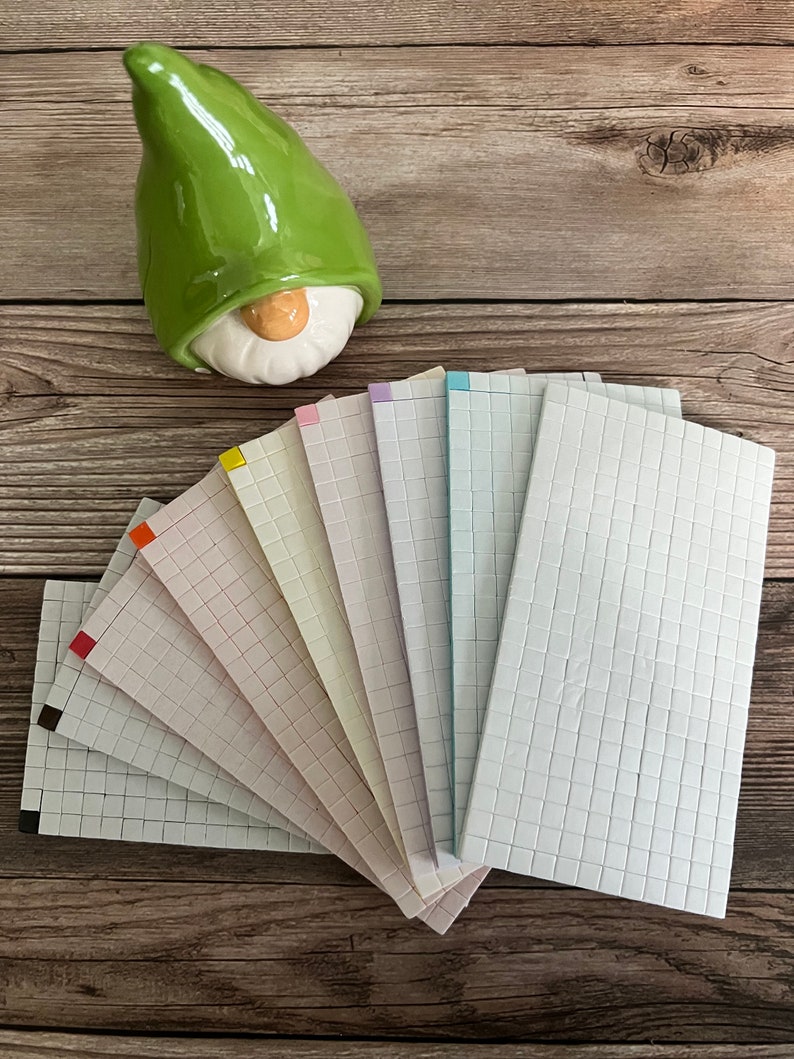 May include: A set of ten white ceramic tiles with a grid pattern. The tiles are arranged in a fan shape and have a variety of colored borders, including red, orange, yellow, light green, pink, purple, blue, and light blue.