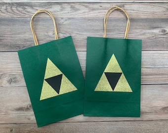 May include: Two green paper gift bags with brown handles. Each bag has a gold glitter triangle with a black triangle inside.