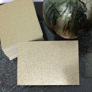 May include: A stack of gold glitter cardstock. The cardstock is smooth and has a subtle shimmer.