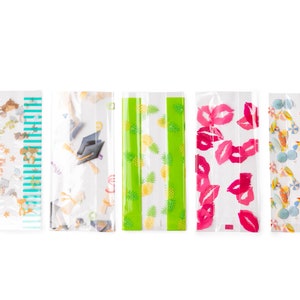 May include: Five clear plastic bags with different printed designs. The designs include a green and white pineapple pattern, a pink and white lips pattern, a blue and white striped pattern with small animals, a white and blue graduation cap pattern, and a white and blue beach themed pattern.