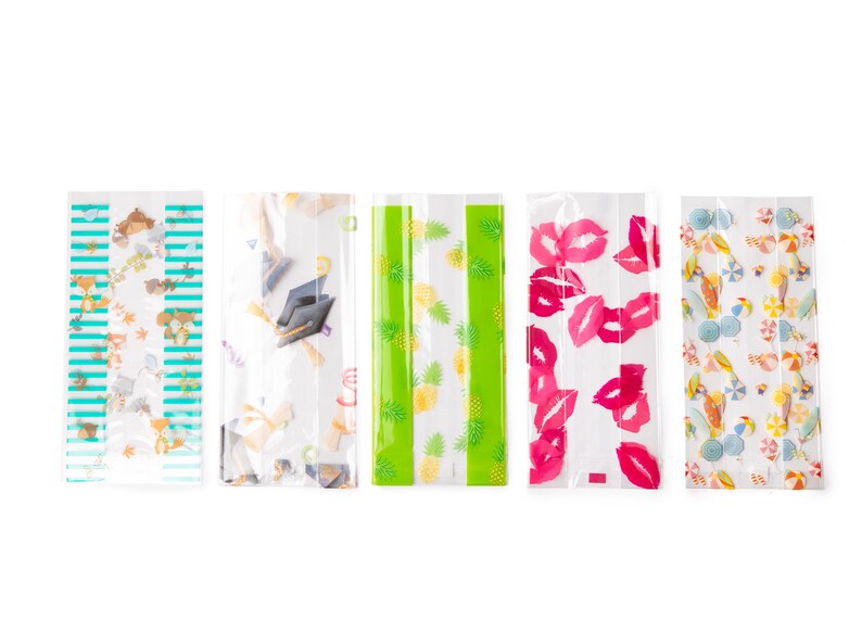 May include: Five clear plastic bags with different printed designs. The designs include a green and white pineapple pattern, a pink and white lips pattern, a blue and white striped pattern with small animals, a white and blue graduation cap pattern, and a white and blue beach themed pattern.