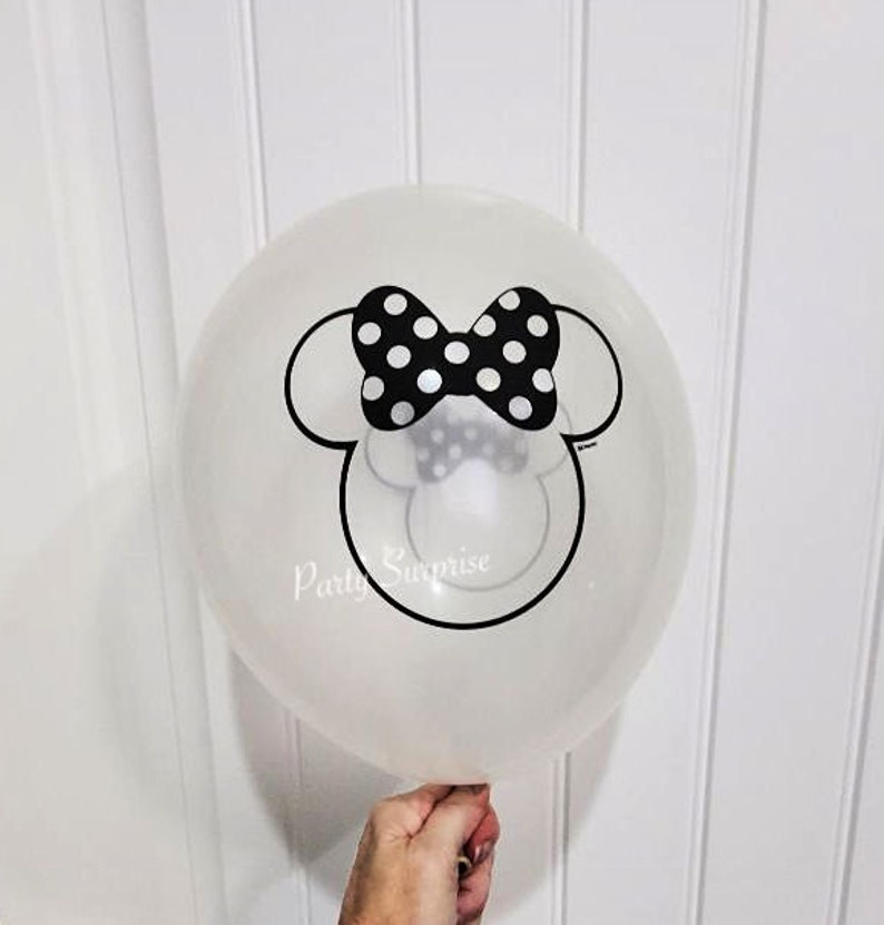 May include: A clear balloon featuring a black and white Minnie Mouse head design. The design includes a black bow with white polka dots and Minnie's signature ears.