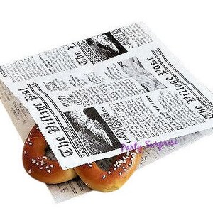 以下が含まれることがあります： 白地の紙袋に、黒と白の新聞柄が印刷された、プレッツェルロールが2つ包まれています。新聞の見出しは「The Village Post」と「1807 Daily News」です。