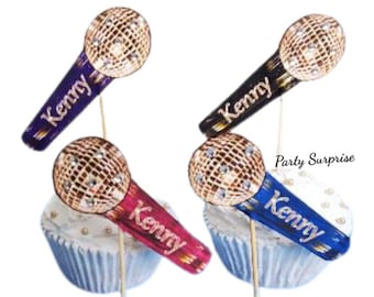 May include: Four microphone-shaped cupcake toppers on thin wooden sticks. Each microphone features a gold-toned, glittery mesh head and a handle in purple, black, pink, or blue, with the name Kenny printed in gold script. The text Party Surprise is visible.