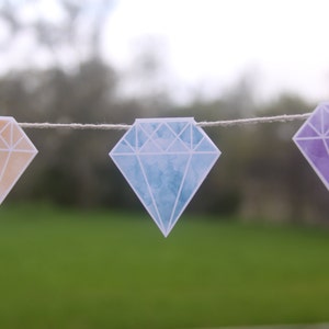 May include: A string of three diamond-shaped paper decorations. The diamonds are in shades of orange, blue, and purple.