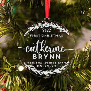 Könnte beinhalten: Runder, transparenter Weihnachtsbaumschmuck mit weißem Text, der "2022 First Christmas catherine BRYNN 9 LBS 3 OZ | 20 IN | 5:13 AM 05.25.22" lautet.