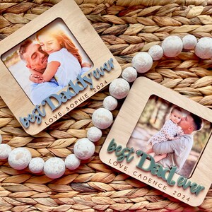 May include: Two wooden photo frames with a light brown wood finish. Each frame has a white mat and a photo of a child with their father. The frames have the text "best Daddy ever" and "best Dad ever" with the child's name and the year 2024.