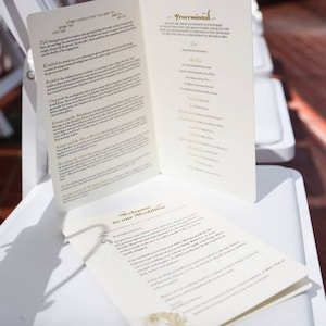 Puede incluir: Un programa de ceremonia de boda con fondo blanco y letras doradas. El programa incluye el orden de la procesión, las lecturas y los himnos. El programa también incluye un mensaje de bienvenida a los invitados.