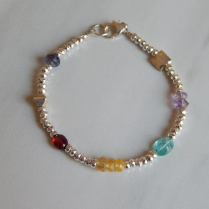 May include: A silver bracelet with a variety of colorful gemstones, including amethyst, garnet, citrine, and aquamarine.