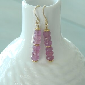 May include: A pair of gold earrings with pink gemstone beads. The earrings are dangle style and have a simple design.