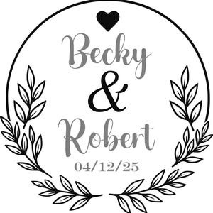 May include: A circular design with the names "Becky & Robert" in gray and black script, a black heart, and the date "04/12/25". The design is framed by a black circle and adorned with leaf branches.
