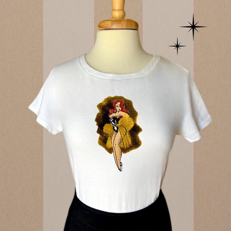 Pu&ograve; includere: Maglietta bianca con una grafica di una donna dai capelli rossi con un vestito giallo e un cappotto di pelliccia.