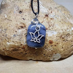 May include: A silver pendant with a gray stone and a silver lotus flower design. The pendant is hanging from a black cord.