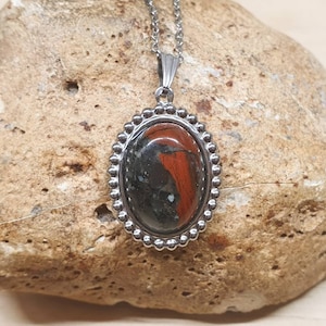 May include: A silver pendant necklace featuring a black and red oval stone set in a silver bezel. The stone has a distinctive pattern of red and black.