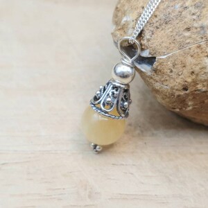 Puede incluir: Un collar con un colgante de plata adornado con una piedra preciosa de color amarillo claro y un dise&ntilde;o de filigrana de plata.