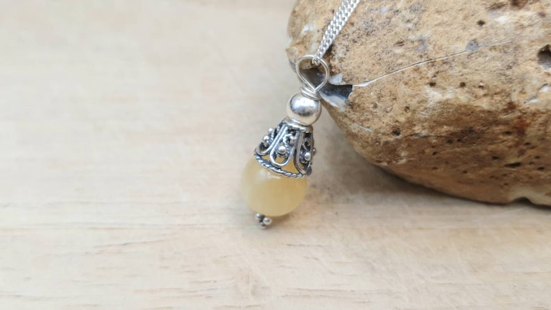Puede incluir: Un collar con un colgante de plata adornado con una piedra preciosa de color amarillo claro y un dise&ntilde;o de filigrana de plata.