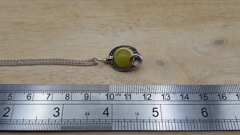 May include: A silver necklace with a green stone pendant. The pendant is round and has a silver swirl design. The necklace is 11 inches long.