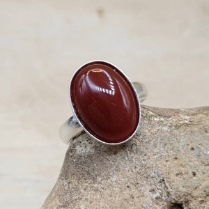May include: A silver ring with a red oval carnelian gemstone