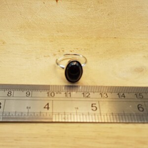 May include: A silver ring with a black oval gemstone. The ring is shown next to a ruler, with the gemstone measuring approximately 1.2 cm in diameter.
