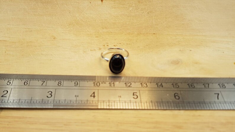 May include: A silver ring with a black oval gemstone. The ring is shown next to a ruler, with the gemstone measuring approximately 1.2 cm in diameter.