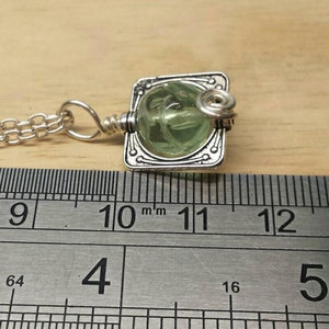May include: A silver chain necklace with a pendant featuring a green glass cabochon set in a silver frame. The pendant is approximately 1.1 inches wide.