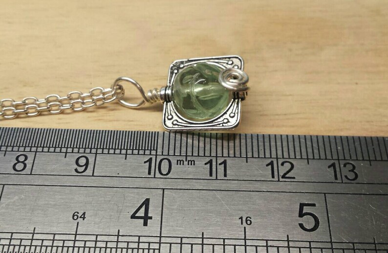 May include: A silver chain necklace with a pendant featuring a green glass cabochon set in a silver frame. The pendant is approximately 1.1 inches wide.
