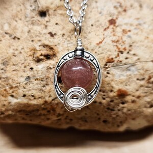May include: A silver necklace with a pink gemstone pendant. The pendant is surrounded by a silver wire design.