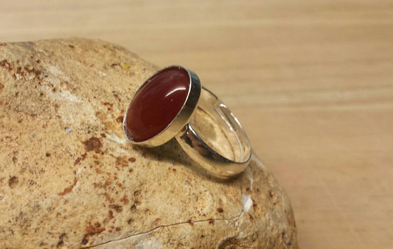 May include: A silver ring with a red carnelian gemstone. The ring is set on a light brown rock.