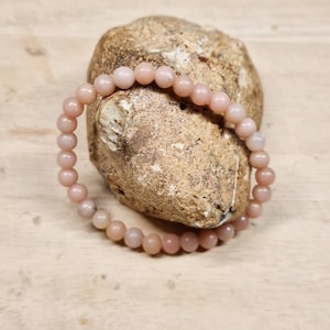 May include: A pink opal beaded bracelet with a natural stone look. The bracelet is on a light brown wooden surface.