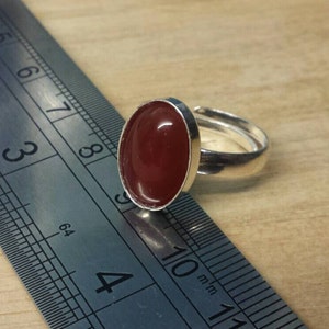 May include: A silver ring with a red oval-shaped gemstone. The ring is shown next to a ruler, with the gemstone measuring approximately 1 inch in length.