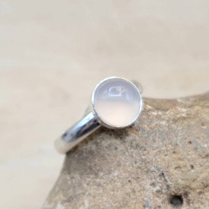 May include: A silver ring with a round, pale pink gemstone.