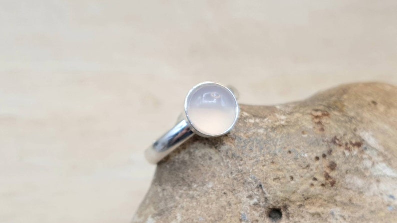 May include: A silver ring with a round, pale pink gemstone.