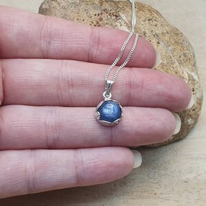 May include: A silver necklace with a blue gemstone pendant. The pendant is set in a silver bezel and has a delicate, ornate design.