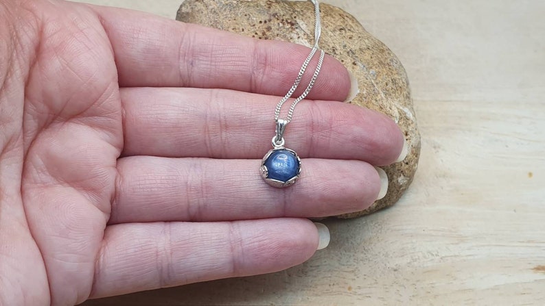 May include: A silver necklace with a blue gemstone pendant. The pendant is set in a silver bezel and has a delicate, ornate design.