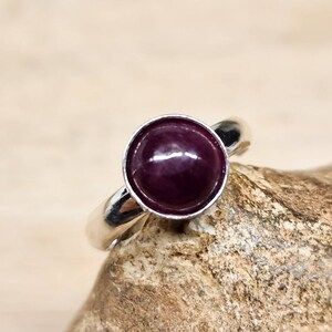 May include: A silver ring with a deep purple gemstone set in a bezel setting.