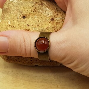 May include: A bronze ring with a round, red carnelian gemstone set in a bezel setting.