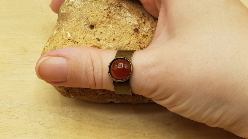 May include: A bronze ring with a round, red carnelian gemstone set in a bezel setting.