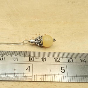 Puede incluir: Un collar de cadena de plata con un colgante de piedra amarilla. El colgante mide aproximadamente 11 mm de di&aacute;metro y tiene un dise&ntilde;o de filigrana de plata.
