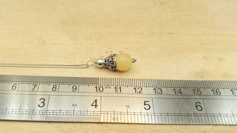 Puede incluir: Un collar de cadena de plata con un colgante de piedra amarilla. El colgante mide aproximadamente 11 mm de di&aacute;metro y tiene un dise&ntilde;o de filigrana de plata.