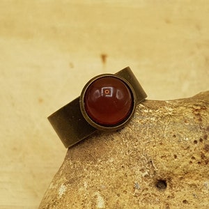 May include: A bronze ring with a round, red carnelian gemstone.