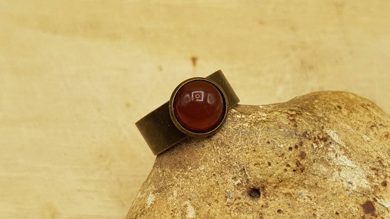 May include: A bronze ring with a round, red carnelian gemstone.