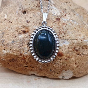 May include: A silver oval pendant necklace with a dark green gemstone set in a beaded bezel.