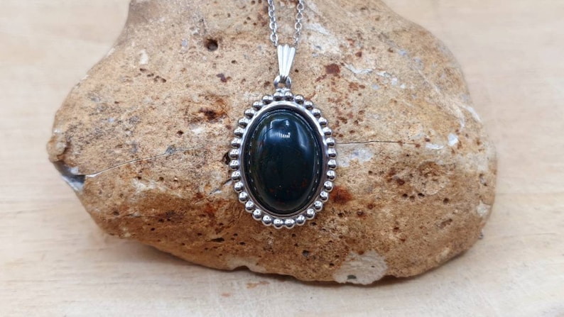 May include: A silver oval pendant necklace with a dark green gemstone set in a beaded bezel.