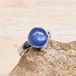 May include: A silver ring with a blue gemstone. The ring is set on a piece of wood.