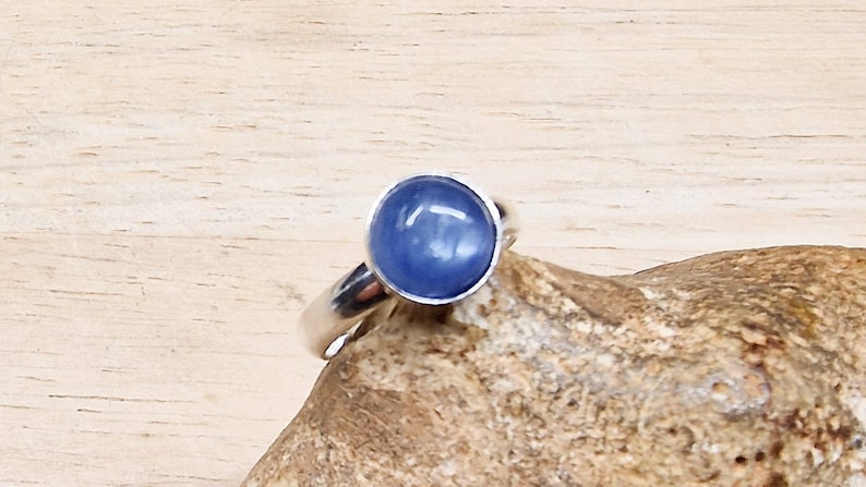 May include: A silver ring with a blue gemstone. The ring is set on a piece of wood.