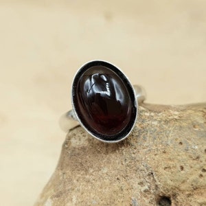 May include: A silver ring with a dark red oval gemstone set in a bezel setting.