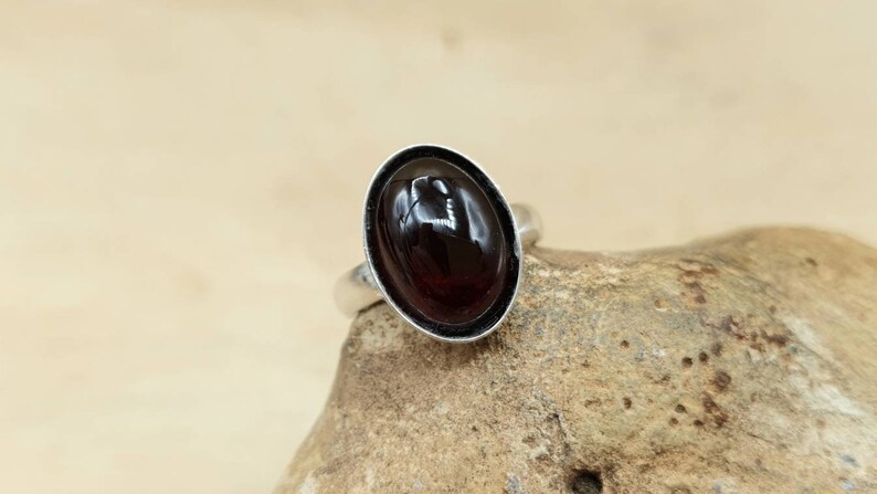 May include: A silver ring with a dark red oval gemstone set in a bezel setting.
