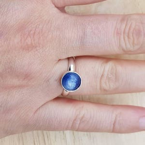 May include: A silver ring with a blue gemstone. The gemstone has a shimmery, iridescent finish.