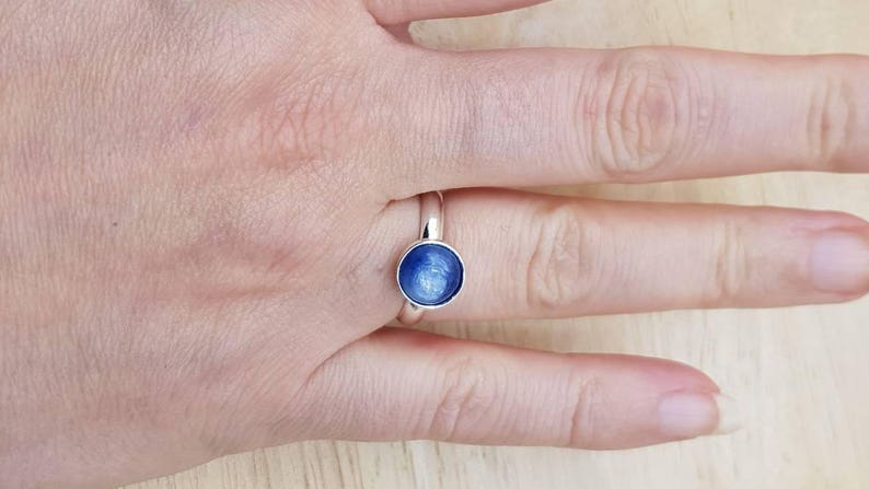 May include: A silver ring with a blue gemstone. The gemstone has a shimmery, iridescent finish.